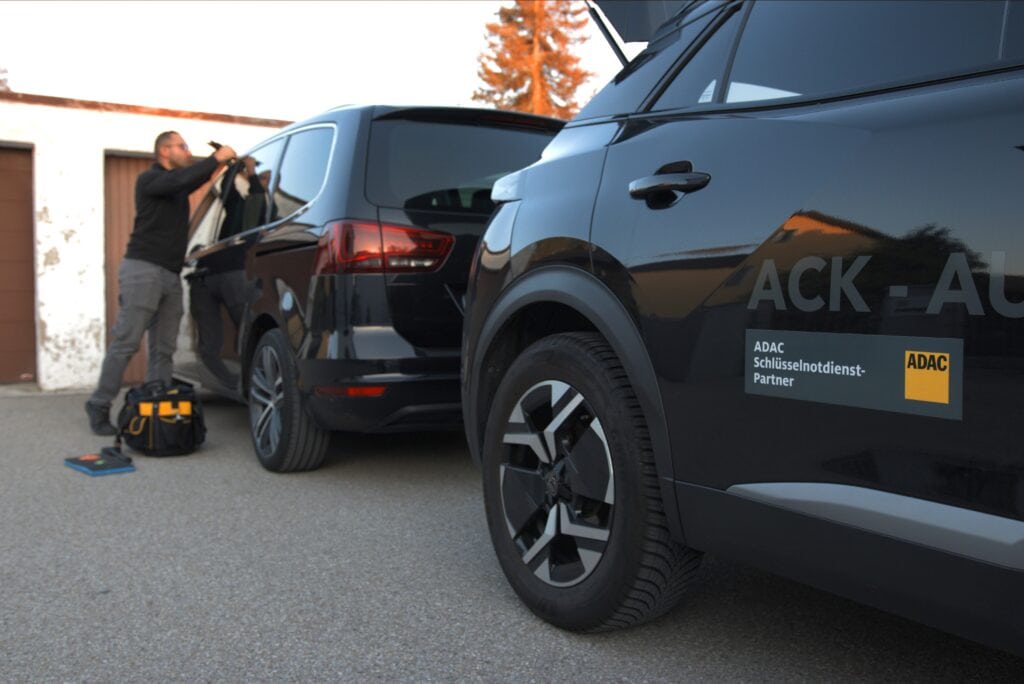 Ein Mann öffnet ein schwarzes Auto; ein zweites Auto mit ADAC-Logo im Vordergrund.